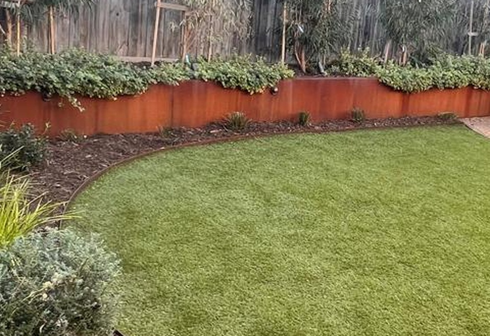 Close-up of weathered Corten steel edging curving around a lawn beneath a rusted Corten raised garden bed