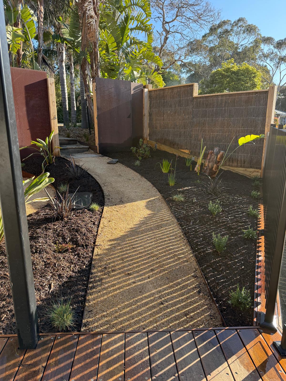 Curved steel edging lining both sides of a crushed-rock garden path between mulched beds