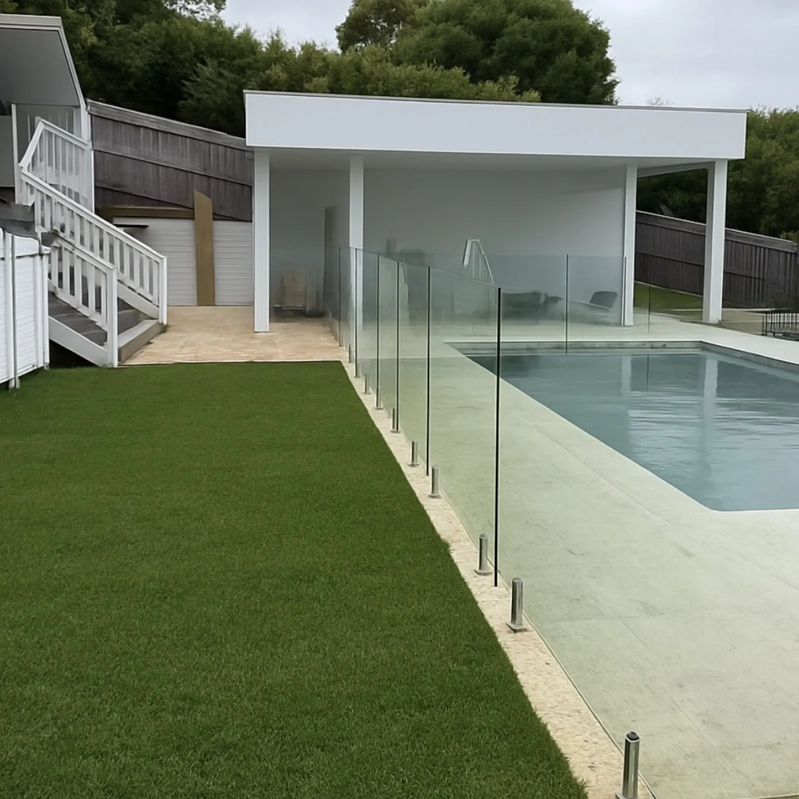 Modern poolside cabana with glass fence and lush lawn